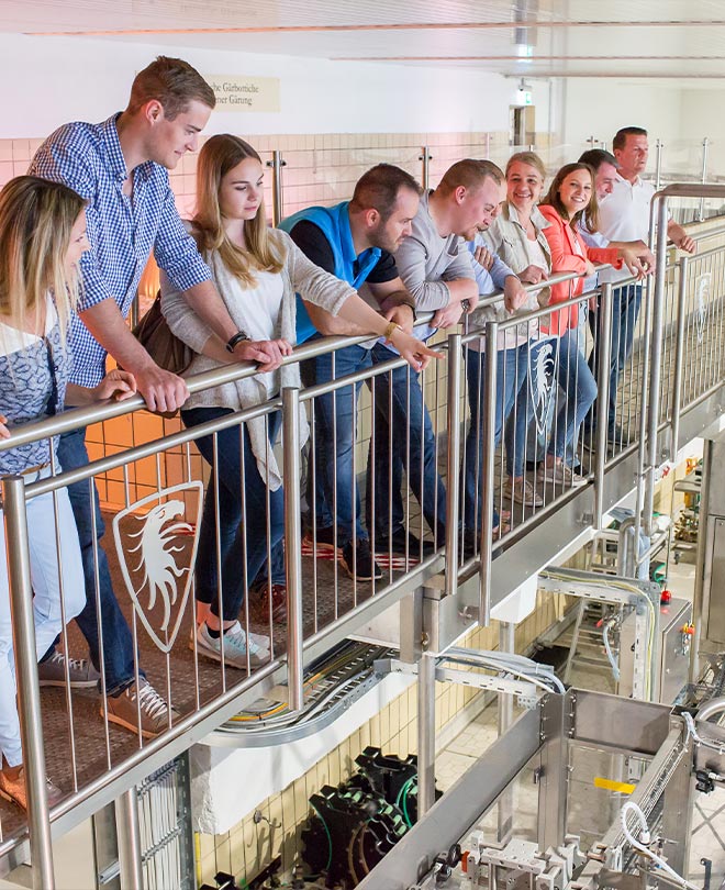 Eine Gruppe von Menschen steht während einer Brauerei-Führungen vor einem Geländer