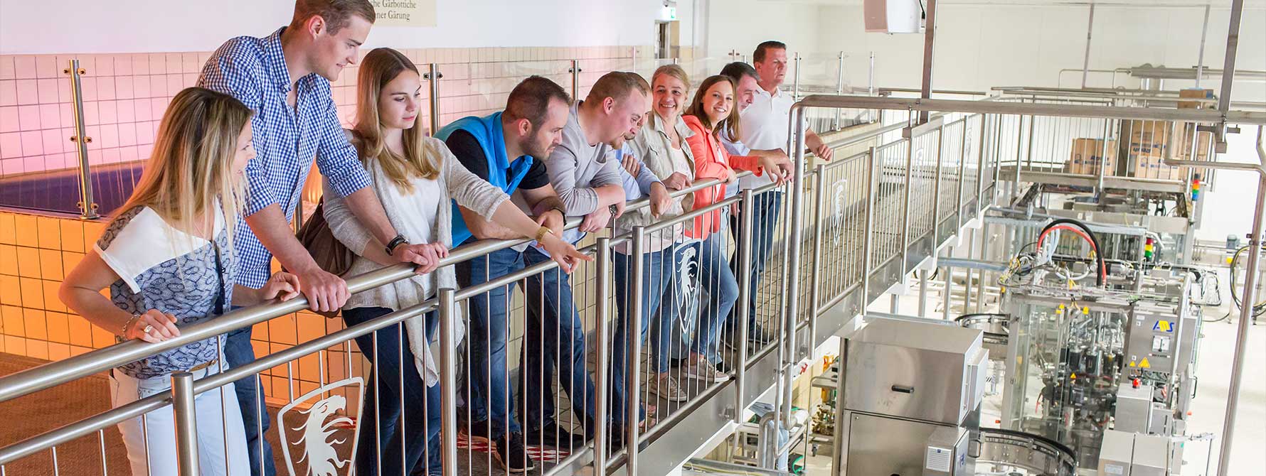 Eine Gruppe von Menschen steht während einer Brauerei-Führungen vor einem Geländer